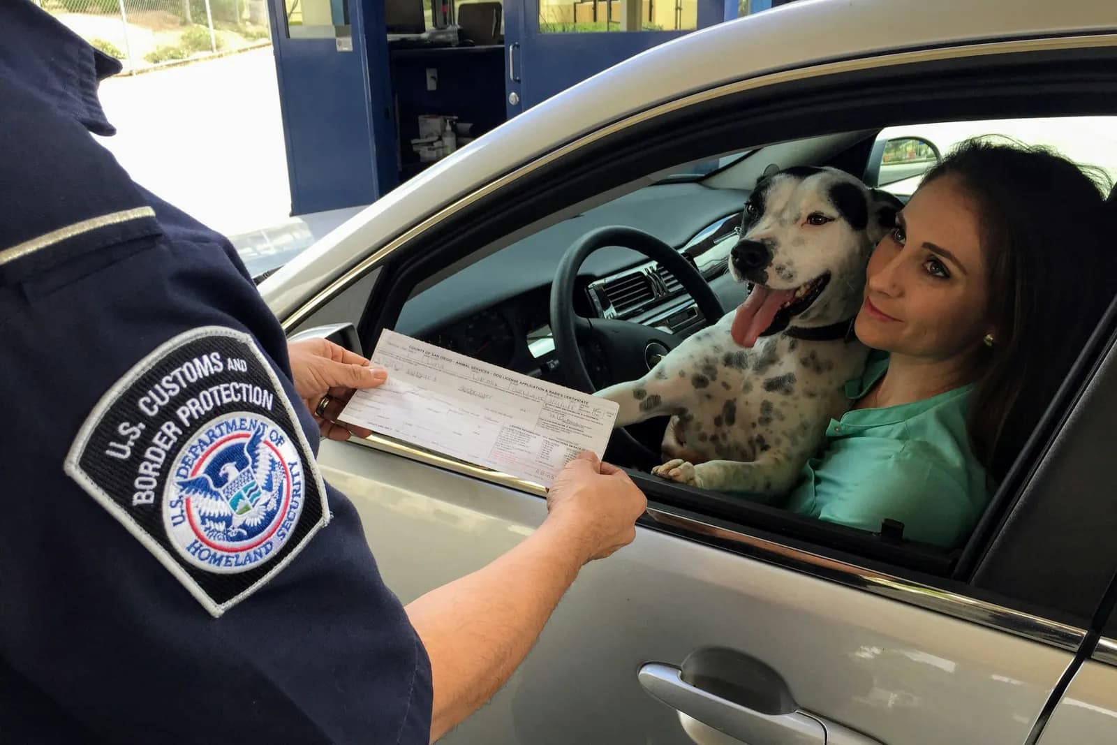 Border officer handing documents to a driver through her car window at a checkpoint
