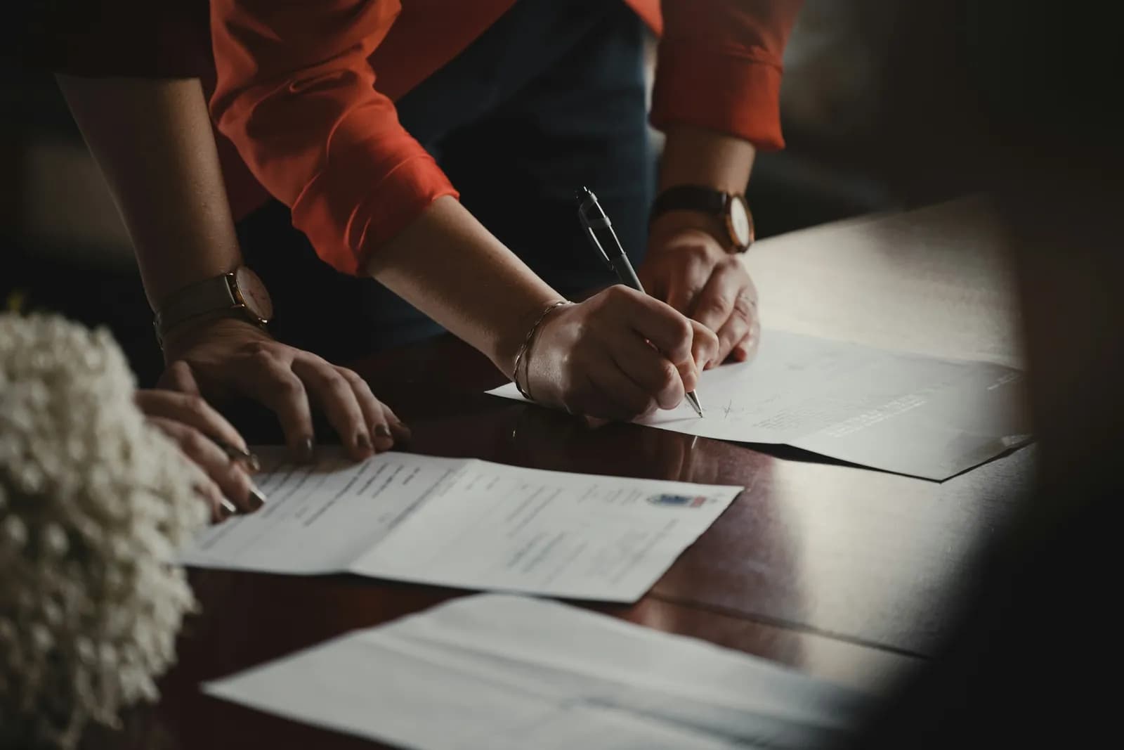 Two people signing a printed contract at a desk, one guiding the pen