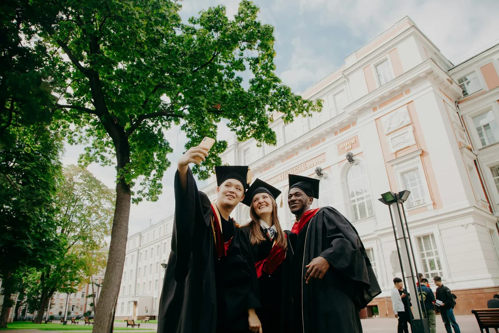 University graduates in caps and gowns taking a selfie outside their faculty building
