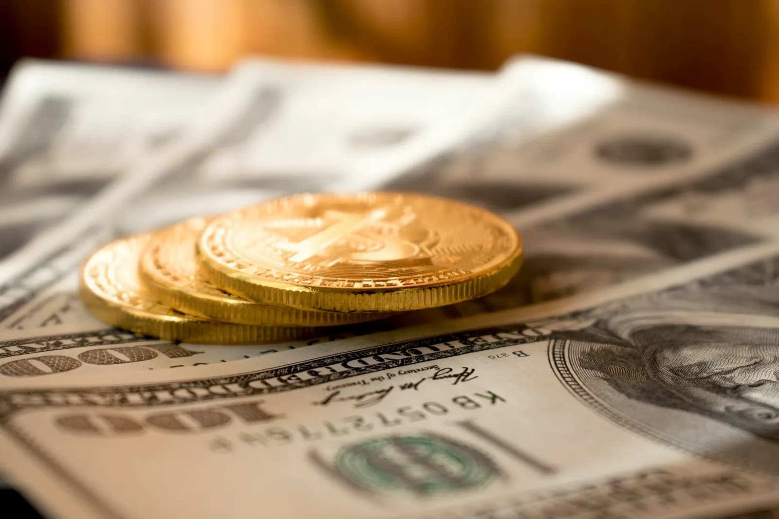 Gold coins resting on a fan of hundred-dollar banknotes