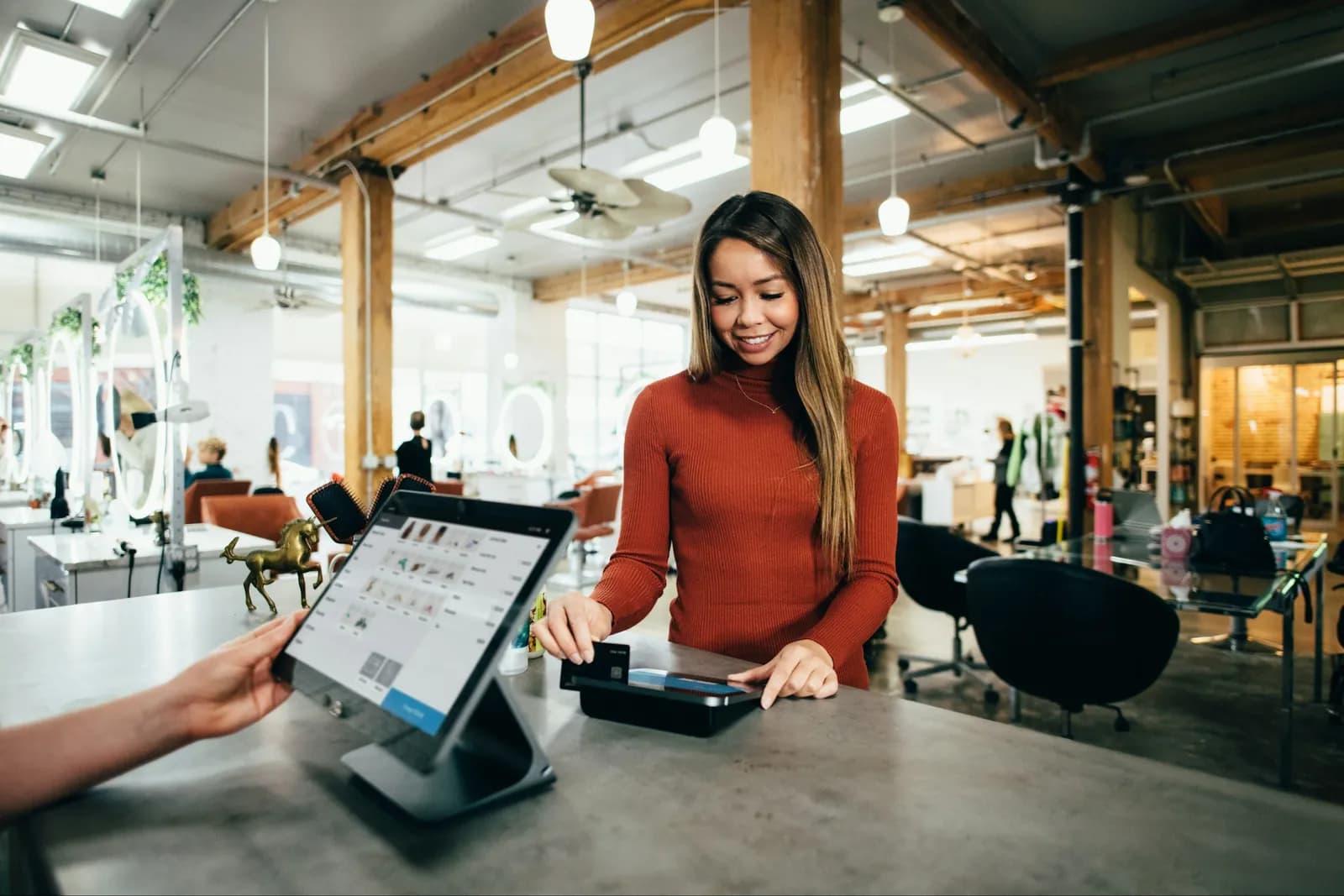 Customer paying by contactless card at a shop counter while staff holds a tablet till